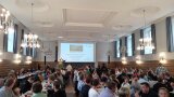 Personen an Tischen in einem Saal