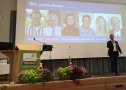 Person steht auf Bühne vor einer Leinwand