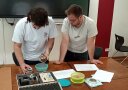 2 Personen stehen vor Unterlagen auf einem Tisch