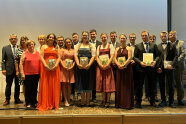 Gruppenbild von Personen in Kleidern und Anzügen auf einer Bühne